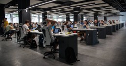 A picture of an office full of people working on laptops