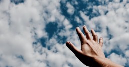 A hand reaching out to a cloudy sky