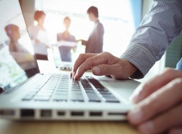 Up close shot of a man on a laptop, with people in the background