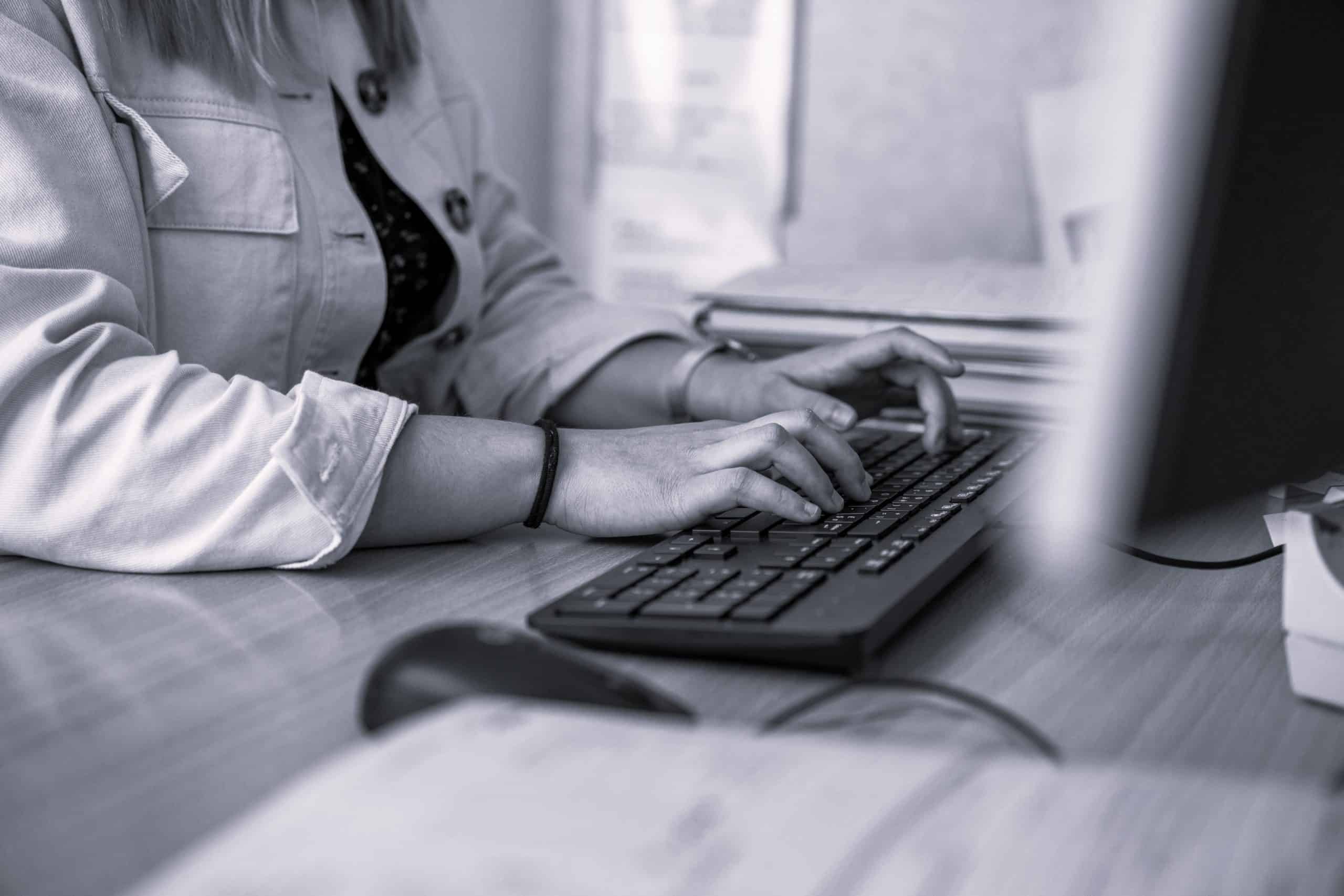 women on computer at desk typing an email on black keyboard