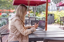 women sitting on phone whilst sat at a table outside using her laptop